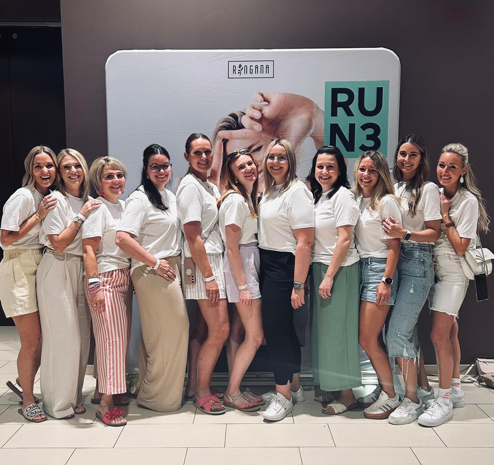Dreizehn Frauen in weißen Shirts stehen nebeneinander vor einer Aufstellwand