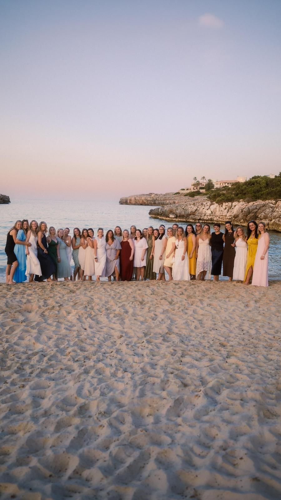Eine große Gruppe Frauen steht bei Abendlicht nebeneinander an einem Sandstrand