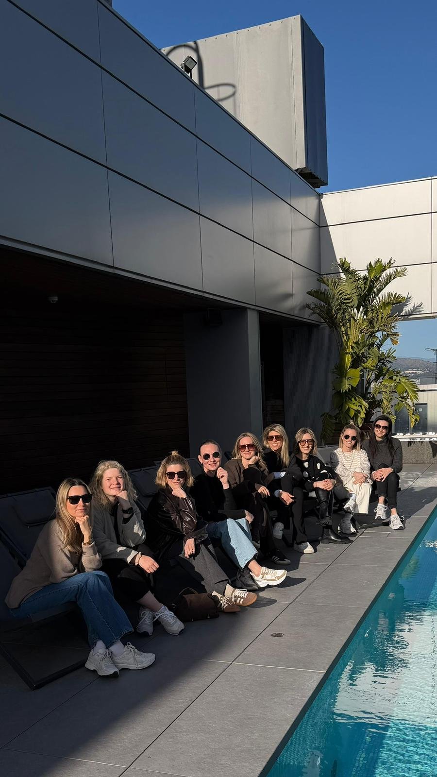 Zehn Frauen sitzen nebeneinander auf einer sonnigen Terrasse an einem Wasserbecken